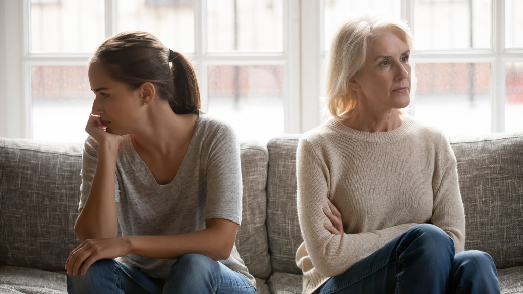 In the fight, the elderly mother, the grown-up daughter sits on the sofa separately, having conflicts, misunderstandings between generations.